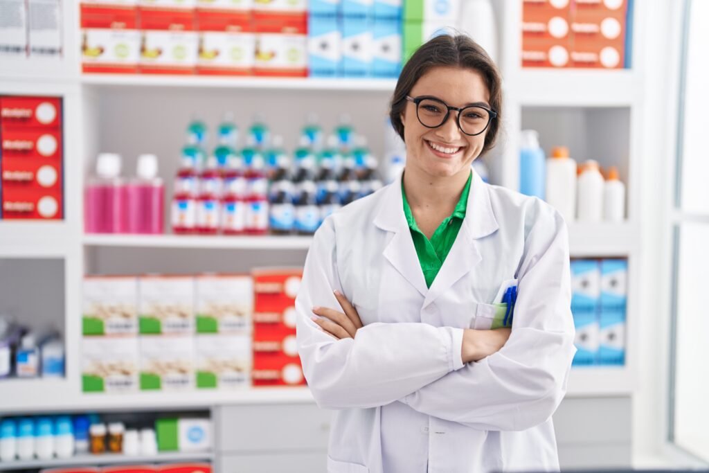 young hispanic woman pharmacist smiling confident standing with arms crossed gesture at pharmacy